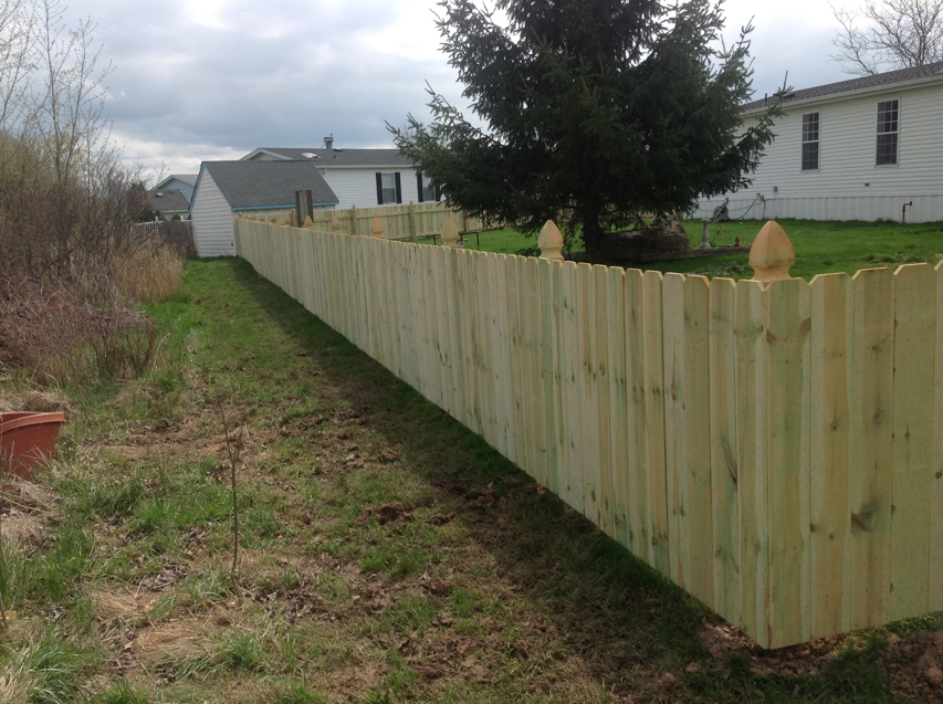 A newly installed wood picket fence in a residential backyard by Woodsmith Fence Corp in Lockport, NY.