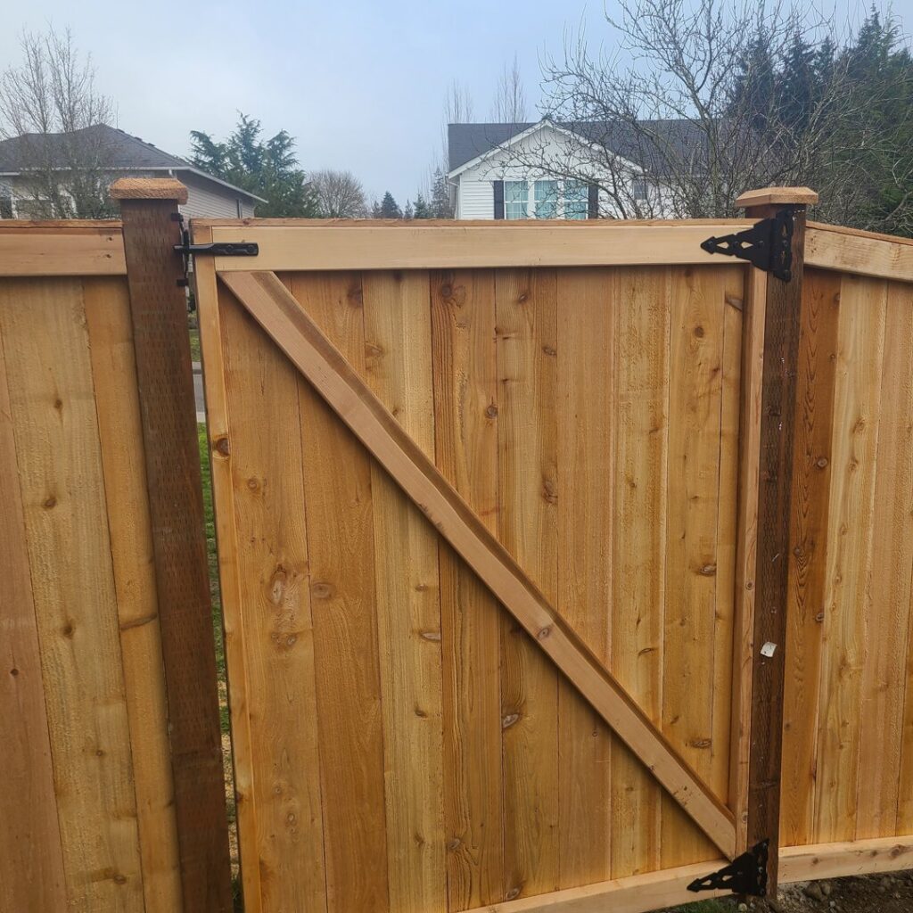 A close-up of a newly installed wooden gate with black decorative hinges by LMS Landscapes & Fence services in Auburn, WA.