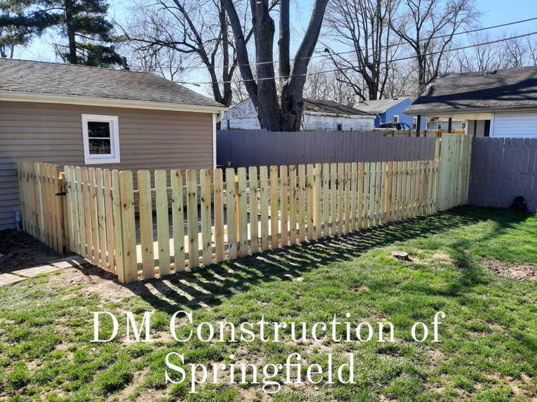 A newly installed wooden picket fence with a gate in a backyard, built by DM Construction of Springfield in Springfield, IL.