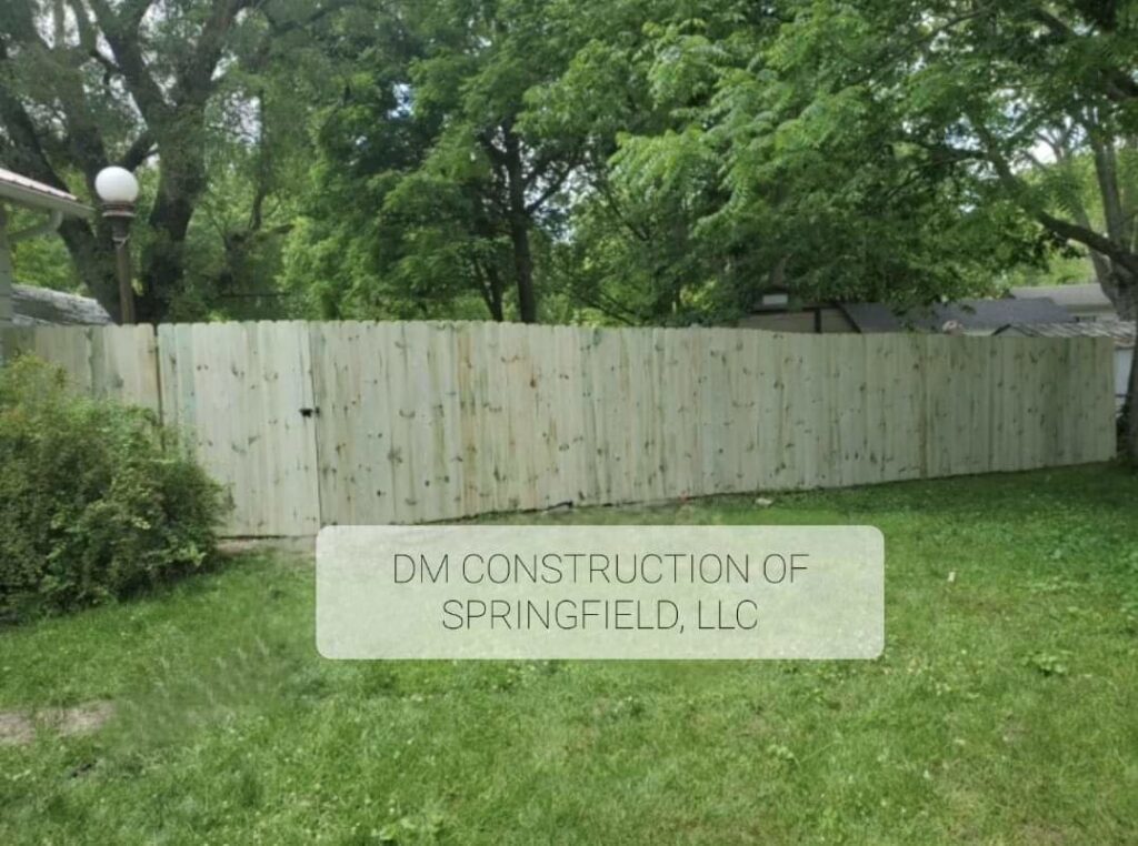 A newly installed tall wooden privacy fence in a green backyard, built by DM Construction of Springfield in Springfield, IL.