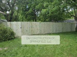 A newly installed tall wooden privacy fence in a green backyard, built by DM Construction of Springfield in Springfield, IL.