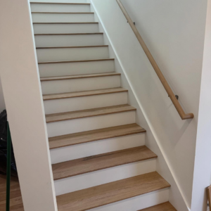 A newly installed wooden staircase with white risers and a handrail by Markos Construction in Cambridge, MA.