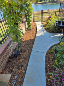 A newly laid concrete pathway next to a brick wall and fence, completed by All American Concrete in Crescent, OK.