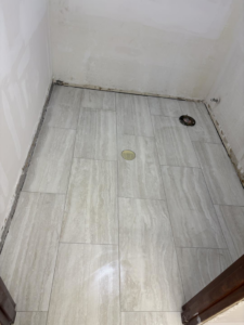 Newly laid light grey floor tiles in a room with unfinished walls by Capitol Construction and Roofing LLC in Raleigh, NC