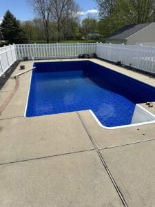 A newly lined swimming pool, filled with water and surrounded by a white fence, by Heatwave Pools LLC in Flint, MI.