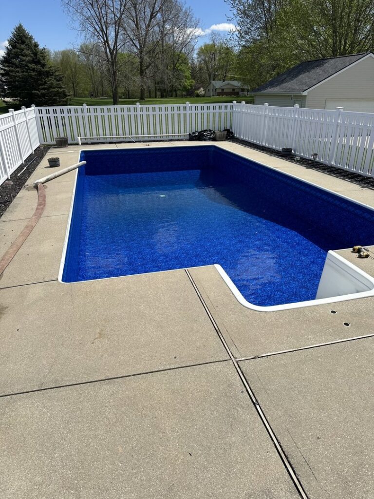 A newly lined swimming pool, filled with water and surrounded by a white fence, by Heatwave Pools LLC in Flint, MI.