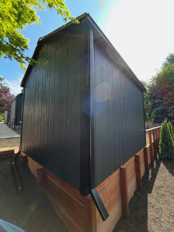 A newly painted dark shed with a new gutter system and wooden retaining wall by Shed Crafters in Sycamore, IL.