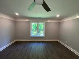 A newly painted room with dark wood flooring and a ceiling fan installed by Rochester Contracting in Holly Springs, NC.