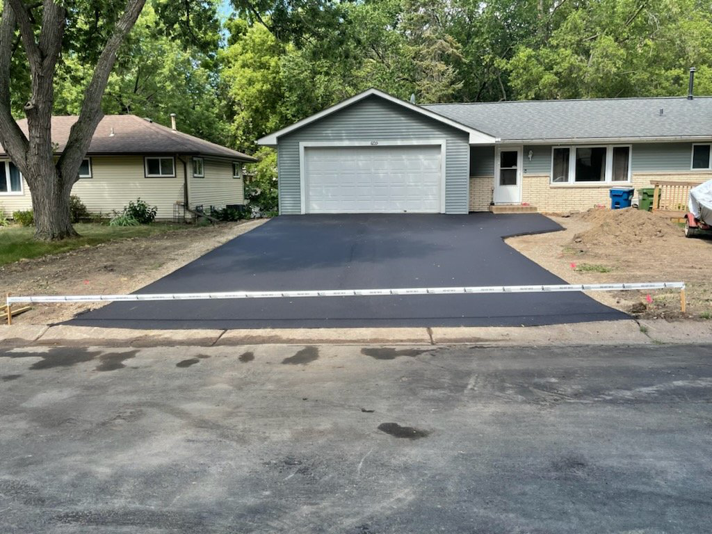 A newly paved asphalt driveway in front of a residential home by First Builders of MN Inc. in Maple Grove, MN