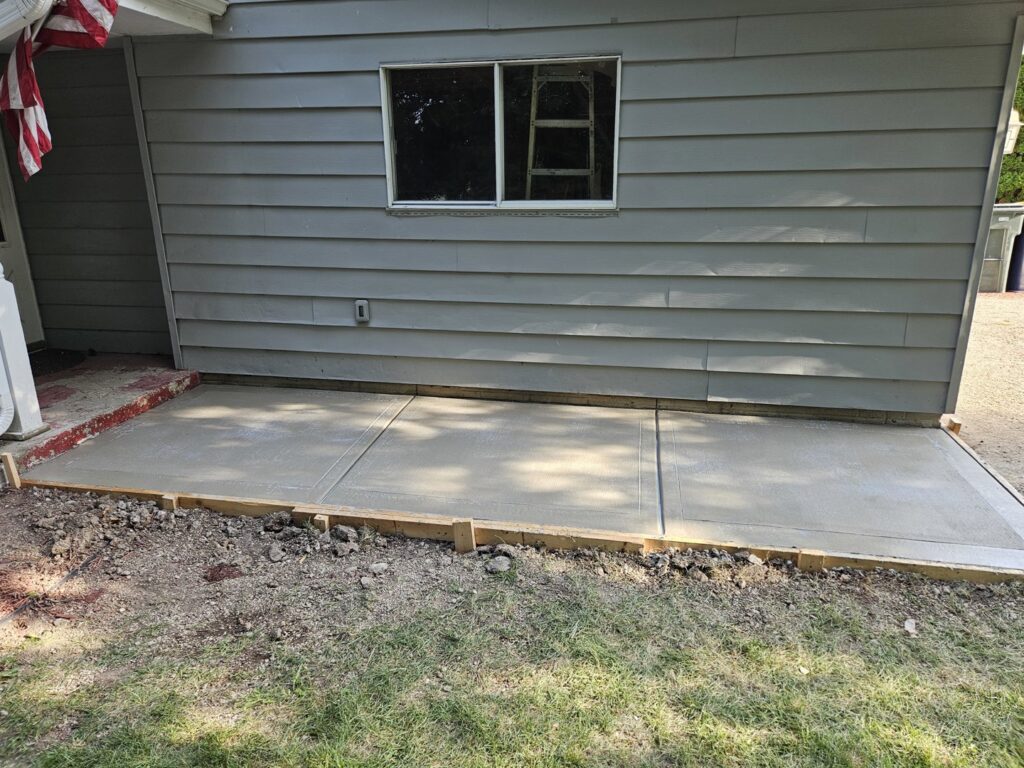 A newly poured concrete patio with wooden forms next to a house by Paramount Development in Milwaukee, WI.