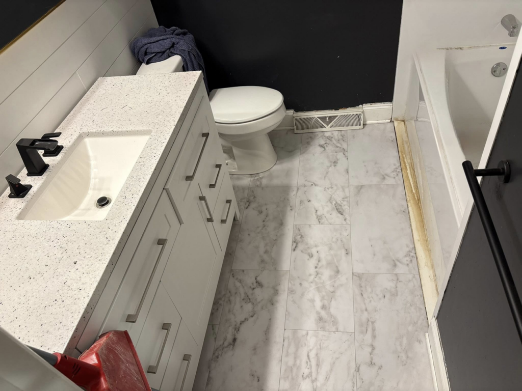 A newly renovated bathroom featuring a new vanity, toilet, and marble-look flooring by CJ Flooring LLC in Flat Rock, MI.