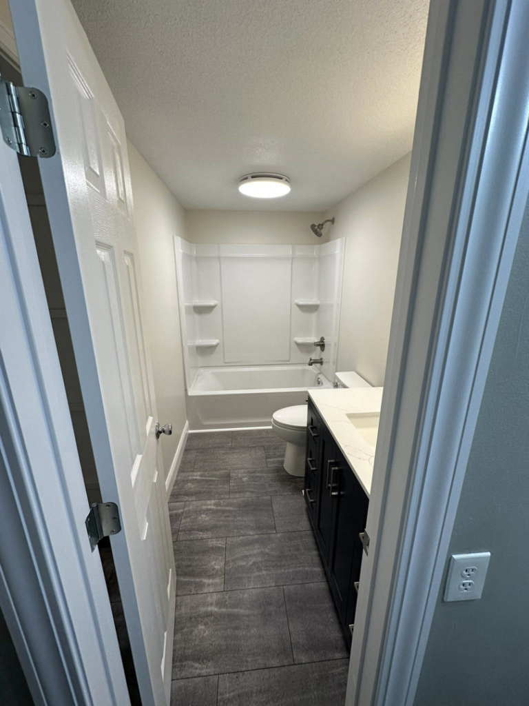 A newly renovated bathroom with a modern vanity, toilet, and shower/tub combo by ThoroughFair Renovations in Lawrence, KS.