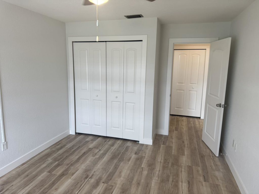 A newly renovated bedroom with light wood-look flooring and white bi-fold closet doors by Bradford Brothers Builders Inc. in Cape Coral, FL