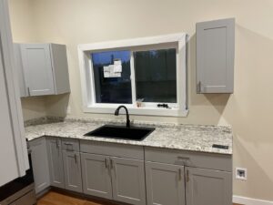 A newly renovated kitchen featuring modern gray cabinets, granite countertops, and a black sink by Guzmanremodeling LlC in Renton, WA.