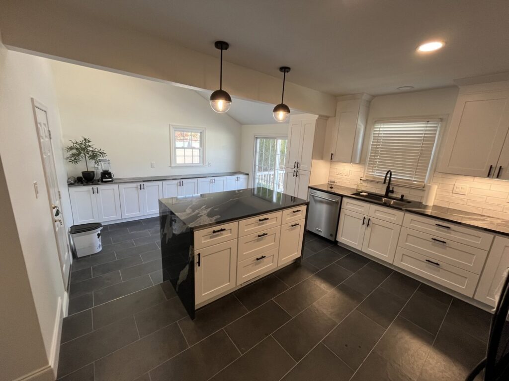 A newly renovated kitchen featuring white cabinets, a large black granite island, and dark tile flooring by MPH Design in Philadelphia, PA.