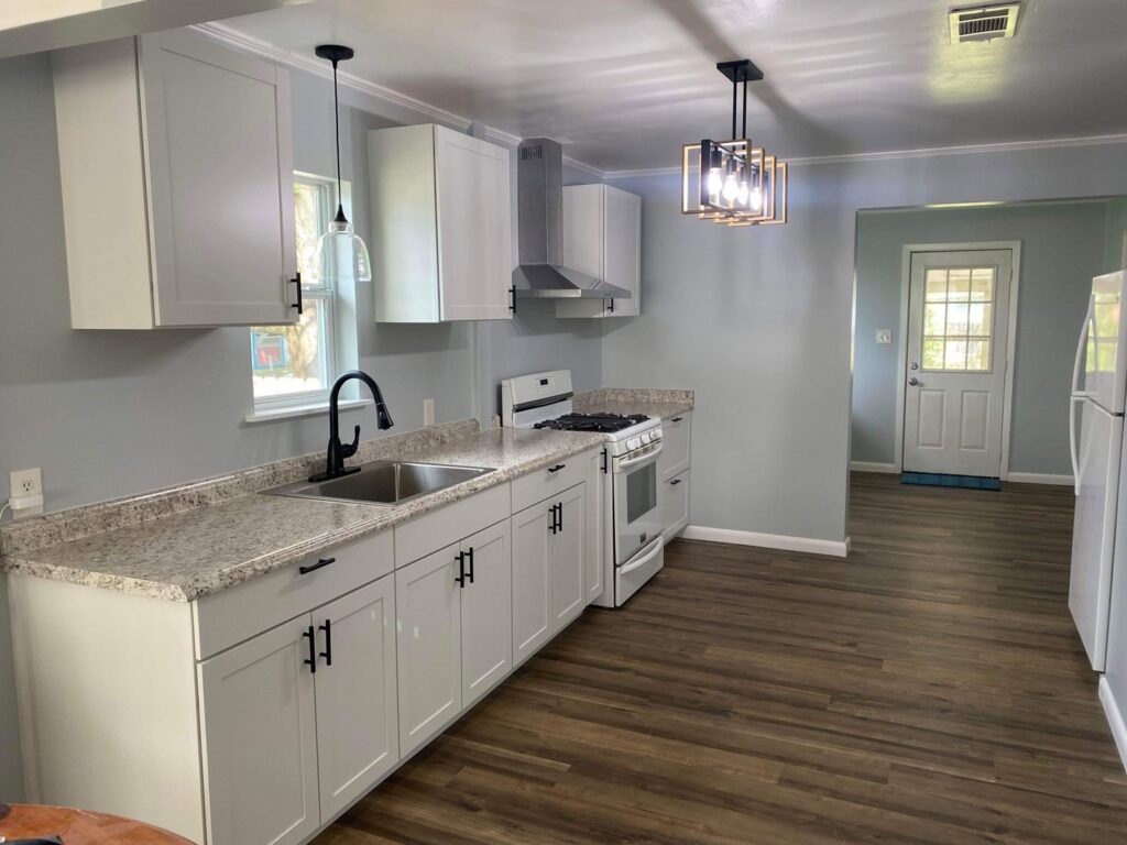 A newly renovated modern kitchen featuring white cabinets, new appliances, and contemporary lighting by SMM Services LLC in Gulfport, MS.