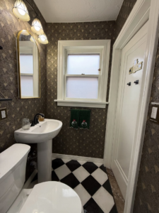 A newly renovated powder room with new wallpaper, pedestal sink, and checkered floor by Waking Up Construction in Oklahoma City, OK.