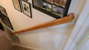 A newly stained wooden handrail expertly installed along a staircase wall by Small Jobs Well Done in Avon, CT.