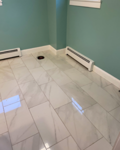 A newly installed white marble-look tile floor in a bathroom with baseboard heaters by Yellow Ladder Contracting in Mount Pleasant, SC