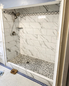 A newly tiled bathroom shower featuring white marble-look tiles and a mosaic floor by Brian's Tiles in Duluth, MN.