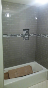 A newly tiled shower and bathtub area with gray subway tiles and a decorative mosaic band by I'll Fix It in Shawnee, KS.
