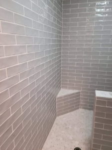 Newly tiled shower enclosure with grey subway tiles, built-in bench, and mosaic floor by Carter's Handyman Service in Bloomington, IN.