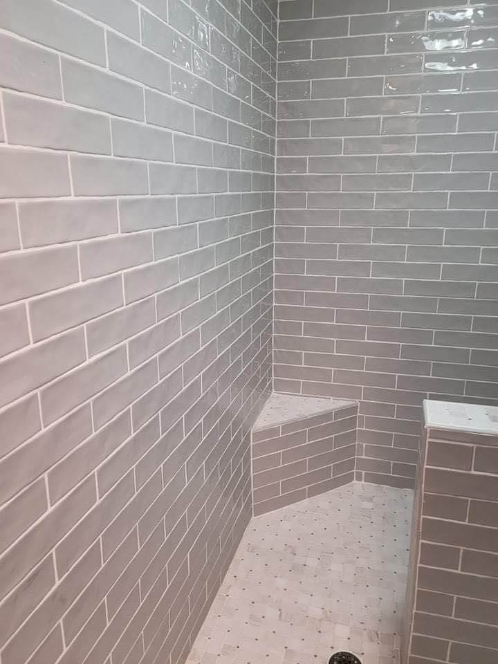Newly tiled shower enclosure with grey subway tiles, built-in bench, and mosaic floor by Carter's Handyman Service in Bloomington, IN.