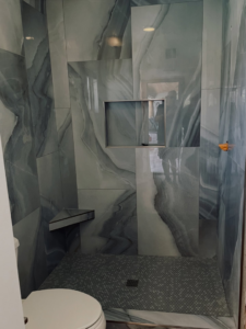 A close-up of a newly tiled shower featuring grey marble-patterned walls and a hexagonal floor by AGM Remodeling LLC in Glendale, AZ.