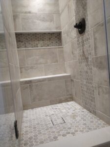 A newly tiled shower with elegant hexagonal floor tiles and a convenient built-in niche, installed by Blas Home Remodeling LLC in New Castle, DE.