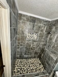 Newly tiled shower with dark grey tiles and a pebble floor and niche by KG Handyman & Remodeling in Vilonia, AR.