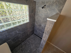 A newly tiled shower remodel with dark grey tiles and a glass block window completed by Next Level Finish in Fort Collins, CO.