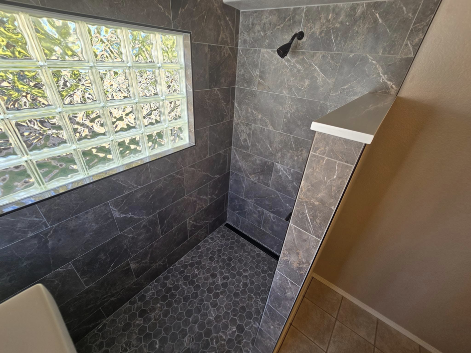 A newly tiled shower remodel with dark grey tiles and a glass block window completed by Next Level Finish in Fort Collins, CO.