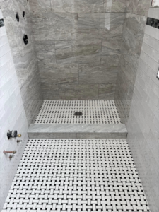 A newly tiled shower stall with grey wall tiles and a basketweave floor by Golden Tile Construction in Yonkers, NY.
