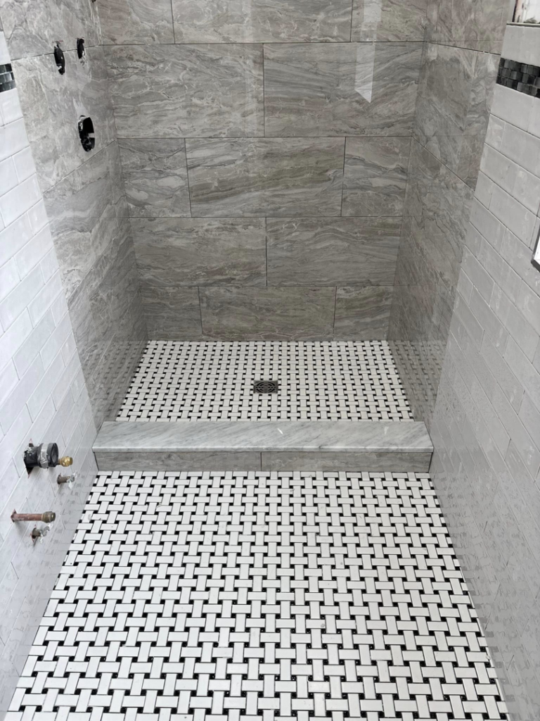 A newly tiled shower stall with grey wall tiles and a basketweave floor by Golden Tile Construction in Yonkers, NY.