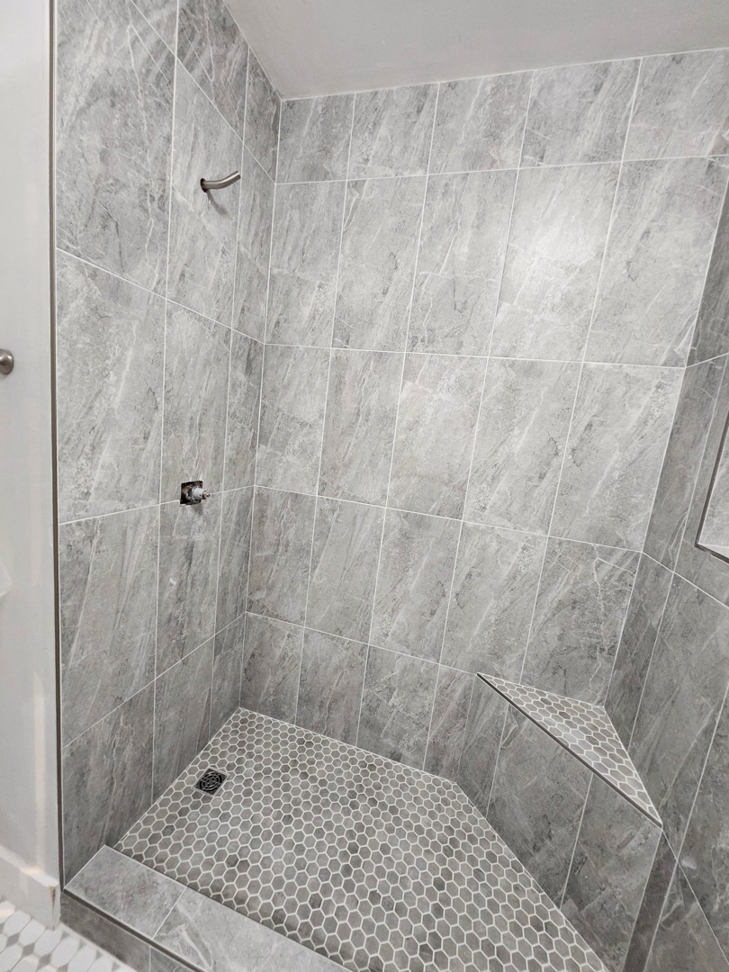 A newly tiled shower stall with grey wall and hexagonal floor tiles by Mr. GreenJeans in Indianapolis, IN.