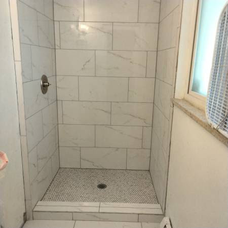 A newly tiled shower stall with white subway tiles and a mosaic floor by True Alchemy - Tile & Grout Restoration in Denver, CO.