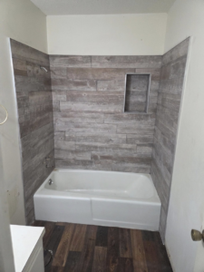 A newly tiled shower surround with wood-look tiles and a bathtub, completed by Joel's flooring & Handyman services in Roy, UT.