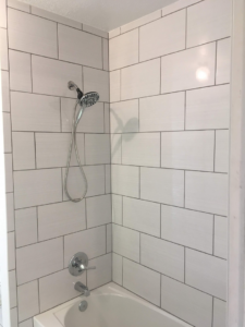 A newly tiled shower surround with white rectangular tiles and a new shower head and faucet installed by OKC Handyman Services in Oklahoma City, OK.