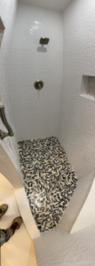 A newly tiled shower featuring textured white wall tiles and a mosaic pebble floor, completed by DG Pro Remodeling in Charlotte, NC