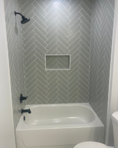 A newly tiled shower and bathtub combination with a gray herringbone pattern and black fixtures by KACE Construction in Nashville, TN.