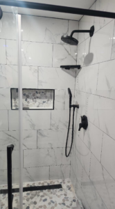 A newly tiled shower with modern black fixtures and a pebble floor installed by Done Right Construction in Johnston, IA.