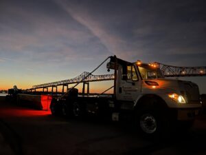 A Vetcans Dumpster Rental truck delivering a red dumpster at night near a bridge in Jacksonville, FL.
