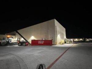 A redbox+ truck picking up a dumpster at night from a commercial building for redbox+ Dumpsters of Greater Austin in Austin, TX