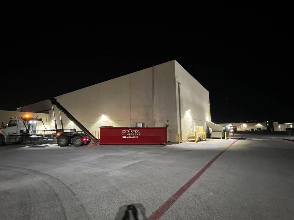 A redbox+ truck picking up a dumpster at night from a commercial building for redbox+ Dumpsters of Greater Austin in Austin, TX