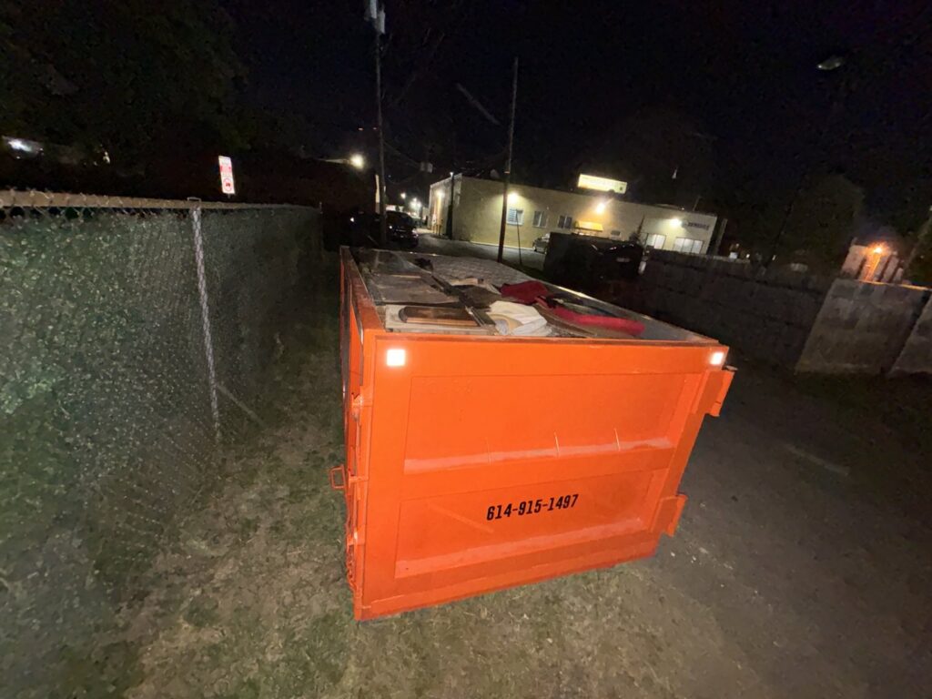 A Crazy Larry's Dumpster Rental container filled with various junk items during a nighttime removal job in Columbus, OH.