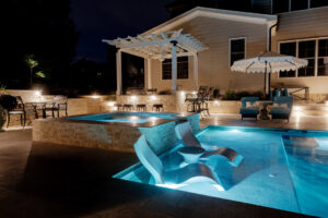 An illuminated night scene of a pool, hot tub, and pergola by Extreme Pools Renovation in Raleigh, NC.