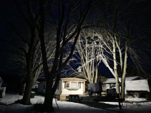 A bucket truck with lights illuminates a tree during night tree removal service by Robert Burk Tree & Landscaping LLC in Milford, DE.