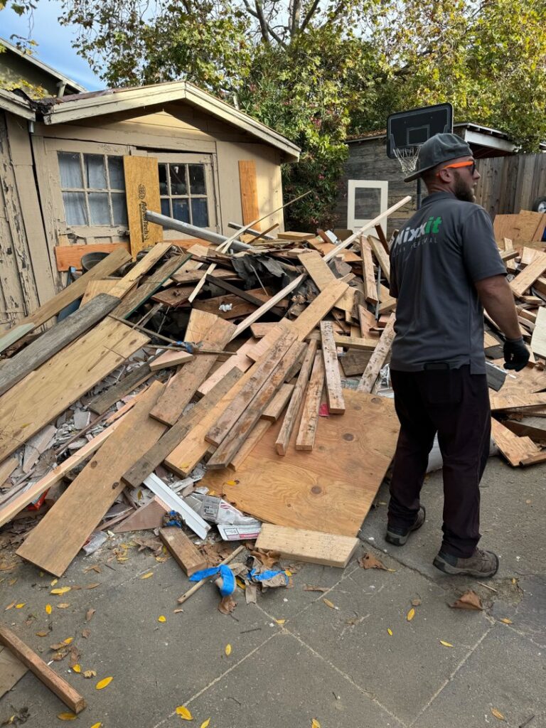 A Nixxit Junk Removal employee standing next to a large pile of wood and construction debris in a backyard in Castro Valley, CA.