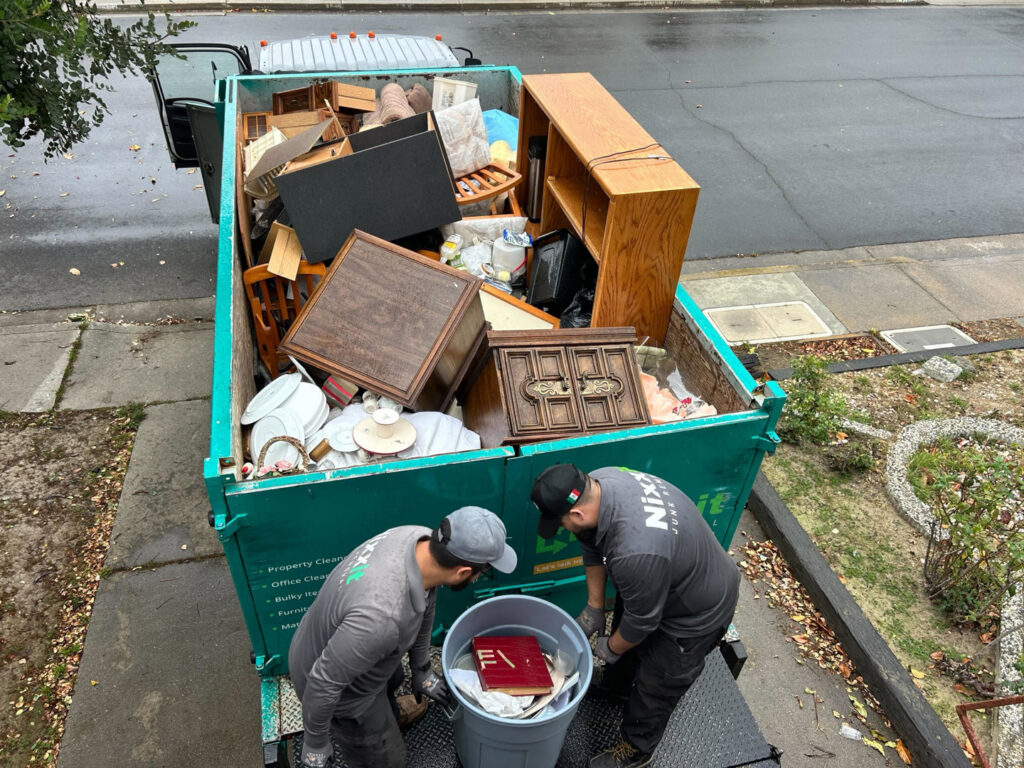 Nixxit Junk Removal employees loading a trash can into a truck already filled with furniture and various junk in Castro Valley, CA.