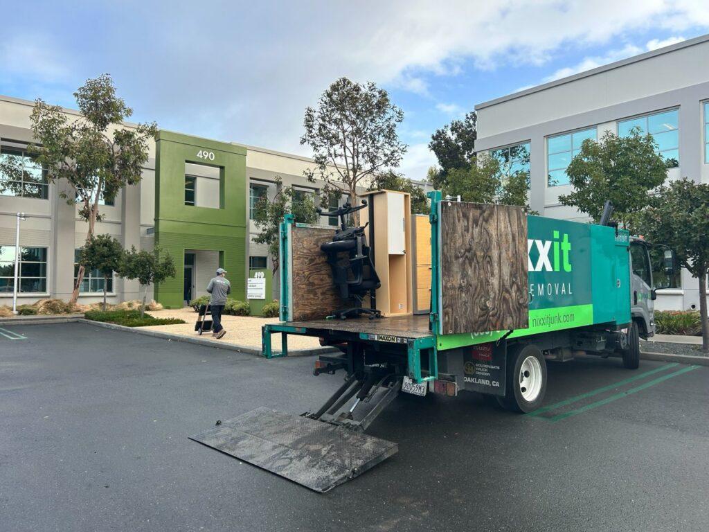 A Nixxit Junk Removal truck loaded with office furniture and other items outside a commercial building in Castro Valley, CA.